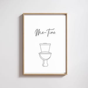 Könnte beinhalten: Gerahmter Druck mit einer minimalistischen Strichzeichnung einer Toilette. Die Worte "Me-Time" sind in einer kursiven Schriftart über der Toilette geschrieben. Der Rahmen ist hellbraun.
