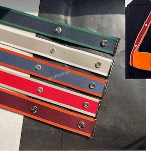 Peut inclure: Une sélection de sangles de sac tissées colorées de différentes couleurs, dont le bleu marine, le rouge et le vert, avec une quincaillerie argentée. Les sangles sont présentées avec un sac orange et une sangle assortie.