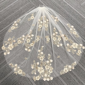 May include: Ivory wedding veil with floral embroidery. The veil is made of sheer fabric and features delicate, embroidered flowers in a complementary color. A comb is attached at the top for secure placement in the hair.