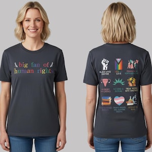 May include: A dark grey t-shirt with the words "big fan of human rights" in rainbow colours on the front. The back displays various graphics and phrases supporting human rights.