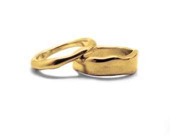 May include: Two gold rings with an irregular, organic shape. The rings are stacked on top of each other.