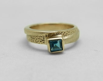 May include: A gold ring with a textured band and a square blue gemstone.