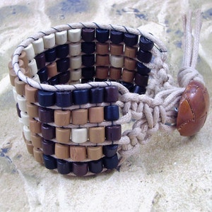May include: A multi-colored wooden bead bracelet with a brown leather button closure. The bracelet is made with brown, black, and cream colored beads.