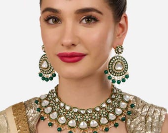 May include: A gold-toned jewelry set featuring a necklace, earrings, and a headpiece. The set includes white, teardrop-shaped stones, green accents, and small green beads. The necklace and earrings have a circular design, and the headpiece is a circular pendant.