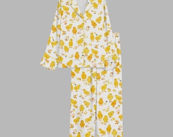 May include: White pajama set with a repeating pattern of yellow chicks and brown leaf shapes. The top has a collared neckline and button-down closure. The pajama pants have a straight leg design. The trim is yellow.