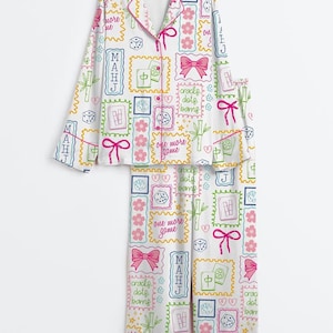 Puede incluir: Conjunto de pijama blanco de manga larga con un estampado colorido de fichas de Mahjong, dados, tallos de bambú, lazos rosas y flores. El texto "MAHJ", "one more game" y "cracks dots bams" está impreso por todas partes. La camisa tiene cuello.