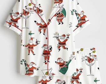 May include: A white short-sleeve button-down pajama shirt and matching shorts set featuring a repeating print of Santa Claus figures holding cocktail glasses, champagne bottles, and candy canes, accented with red piping along the edges.