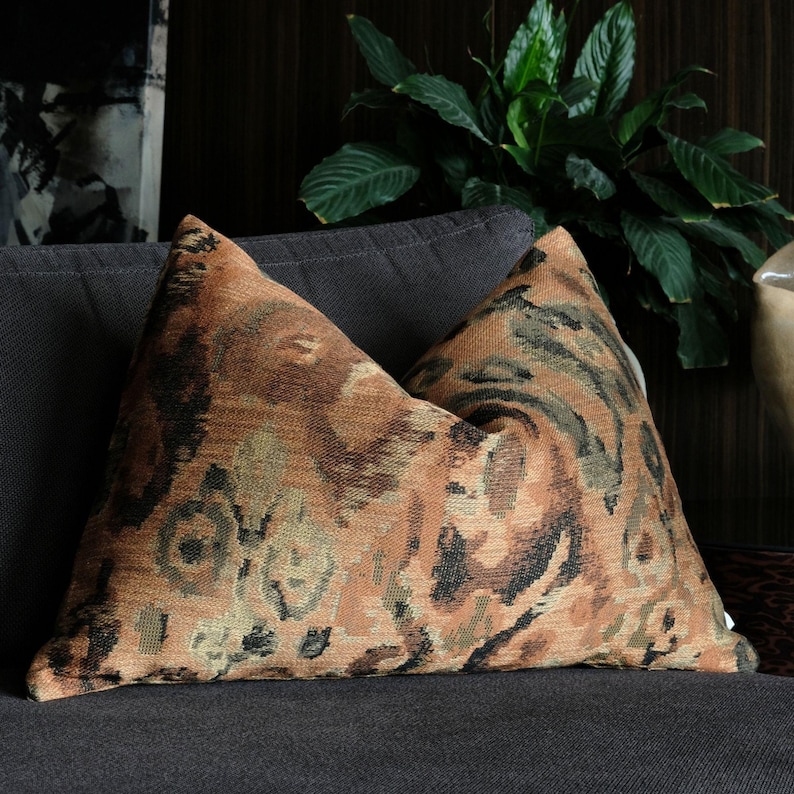 Designer throw pillows in warm rust, olive and earthy tones styled on a dark sofa for contemporary living room decor