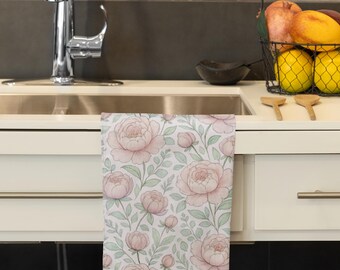 May include: A kitchen towel with a floral pattern of pink peonies and green leaves on a white background. The towel is hanging over a sink in a kitchen setting. The design features large, detailed flowers and delicate foliage.