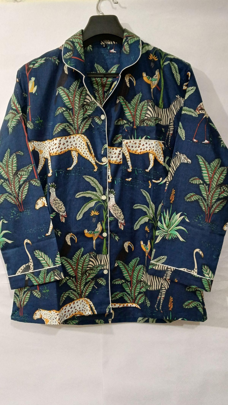 Puede incluir: Camisa de pijama azul marino con estampado de jungla. La camisa de manga larga tiene ribetes blancos y cierre de botones. El estampado incluye leopardos, cebras, loros, flamencos y palmeras.