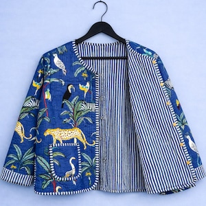 Może przedstawiać: Niebieska pikowana kurtka z żywym nadrukiem w dżungli przedstawiającym lamparty, ptaki i palmy. Kurtka ma podszewkę w paski i zapięcie na guziki. Wisi na czarnym wieszaku.