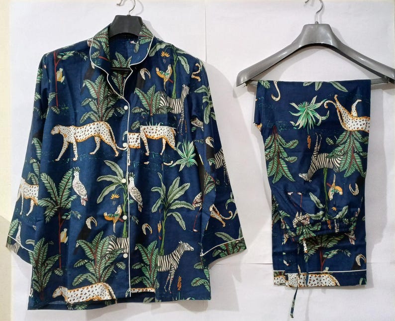 Puede incluir: Conjunto de pijama azul marino con estampado de animales de la jungla. El conjunto incluye una camisa con botones y pantalones a juego, ambos con un estampado de leopardos, cebras y follaje tropical. Ribete blanco.