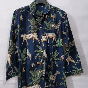 Puede incluir: Top de pijama azul oscuro con estampado de animales de la jungla con leopardos, cebras y loros. La parte superior de manga larga tiene ribetes blancos a lo largo del cuello, los pu&ntilde;os y la tapeta de los botones. La tela tiene un estampado de palmeras y otro follaje tropical.