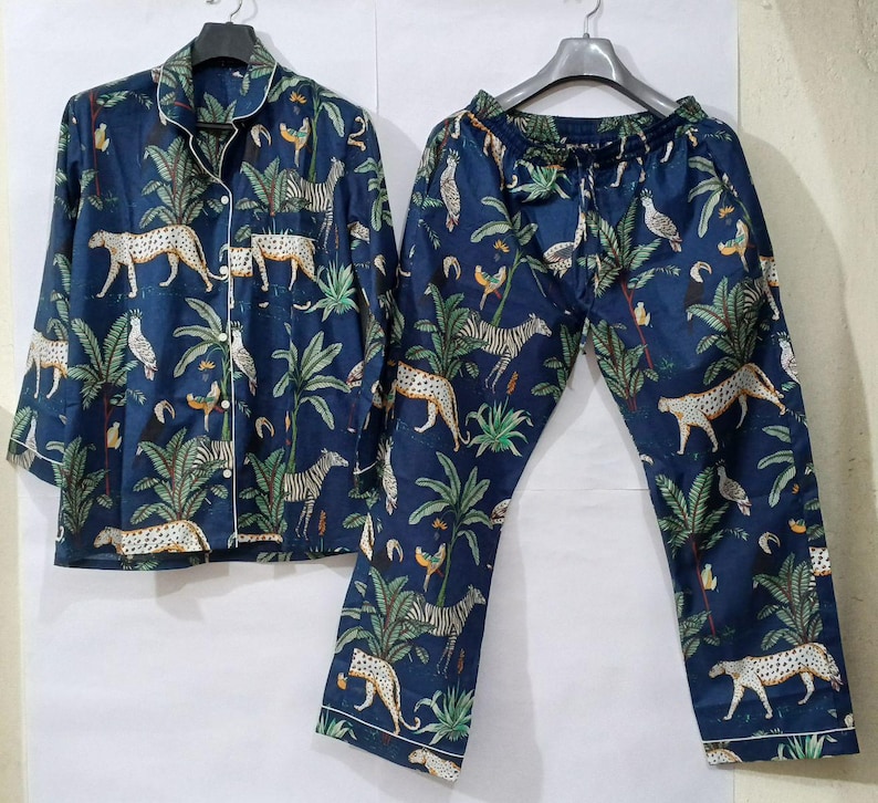 Puede incluir: Conjunto de pijama azul marino con estampado de animales de la jungla. El conjunto incluye una camisa con botones y pantalones a juego. El estampado presenta cebras, leopardos, p&aacute;jaros y follaje tropical.