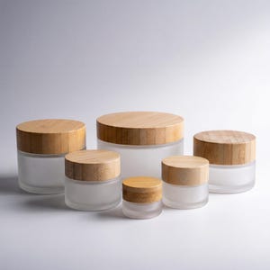 Pode incluir: Uma coleção de frascos de vidro fosco com tampas de bambu natural. Os frascos variam em tamanho, oferecendo uma variedade de opções de armazenamento. As tampas são de cor castanho claro e os frascos têm uma estética limpa e minimalista. Medidas em centímetros.