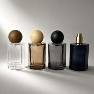 May include: Four hexagonal glass perfume bottles arranged in a row. The first is clear with a dark wood sphere cap, the second is amber with a light wood sphere cap, the third is gray with a black sphere cap, and the fourth is dark blue with a gold pump.