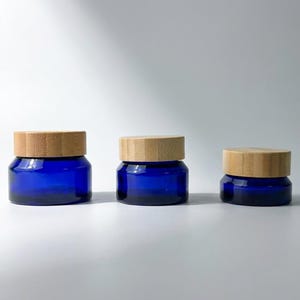 May include: Three cobalt blue glass jars with natural bamboo lids. The jars are arranged in a row, each with a different height. The jars are empty and sit on a white surface.