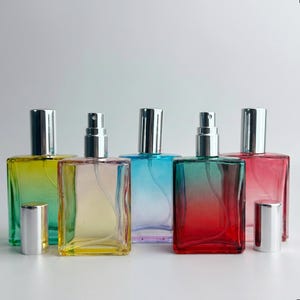 May include: Five rectangular glass perfume bottles with silver spray nozzles and caps. The bottles feature gradient colors including yellow-green, pale yellow, light blue, red-green, and pink-red, each with a clear internal spray tube.