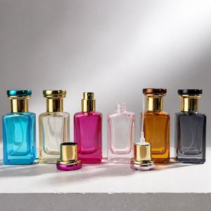 Könnte beinhalten: Eine Sammlung von sechs rechteckigen Glasparfümflaschen mit goldfarbenen Sprühkappen. Die Flaschen sind blau, klar, magentafarben, klar, bernsteinfarben und dunkelgrau. Zwei goldene Kappen sind abgenommen und vor den Flaschen platziert.