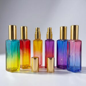 May include: A collection of rectangular glass spray bottles in various colors, including yellow, red, purple, and blue. Each bottle has a gold-colored cap and a matching spray nozzle. The bottles are arranged in a row, showcasing their gradient color schemes.