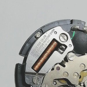 Puede incluir: Primer plano de un movimiento de reloj, con engranajes visibles, una bobina de cobre y una placa plateada. La placa est&aacute; marcada con "PRESTIGE TIME CO LTD SWISS PARTS/MOVEMENT CHINA ONE 1 JEWEL ISA 117".
