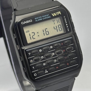 May include: Black Casio digital watch with a calculator-style keypad. The watch face displays the time as 12:16 and the day as TH. Features include water resistance and an alarm. The watchband is black.