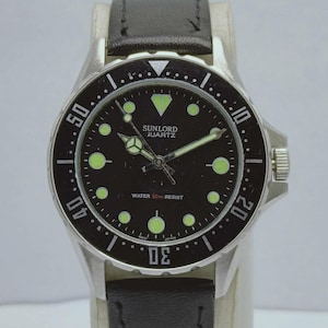 May include: A silver-toned Sunlord Quartz watch with a black dial and a black leather band. The watch face features luminous green markers and hands, with the text "WATER 50m RESIST". The bezel has white numerals and markers.