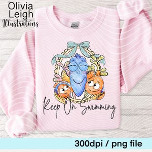 Könnte beinhalten: Ein hellrosa Sweatshirt mit einer Cartoon-Illustration von drei Fischfiguren. Das Design ist von einem Kranz und einer blauen Schleife umrahmt. Die Worte "Keep On Swimming" stehen darunter. Der Text "Olivia Leigh Illustrations" befindet sich oben links.