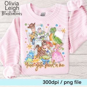 Op de afbeelding: Zachtroze sweatshirt met een kleurrijke illustratie van tekenfilmfiguren, waaronder Woody en Buzz Lightyear. Het ontwerp bevat de zin "You've gotta friend in me". Het sweatshirt heeft ook de tekst "Olivia Leigh Illustrations".