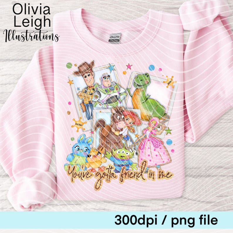 Op de afbeelding: Zachtroze sweatshirt met een kleurrijke illustratie van tekenfilmfiguren, waaronder Woody en Buzz Lightyear. Het ontwerp bevat de zin "You've gotta friend in me". Het sweatshirt heeft ook de tekst "Olivia Leigh Illustrations".