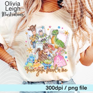 Op de afbeelding: Cr&egrave;mekleurig T-shirt met een kleurrijke afbeelding van Toy Story-personages. Het ontwerp bevat Woody, Buzz Lightyear, Rex en anderen, met de tekst "You've gotta friend in me". Het shirt heeft ook de tekst "Olivia Leigh Illustrations".