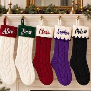 Könnte beinhalten: Fünf personalisierte Weihnachtsstrümpfe mit Zopfstrickmuster. Die Strümpfe haben Bündchen, auf denen die Namen Alice, James, Clara, Sophia und Milo in verschiedenen Farben gestickt sind. Die Strümpfe sind weiß, rot, lila und schwarz mit Aufhängeschlaufen.