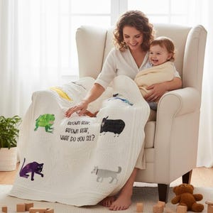 May include: A white quilted blanket featuring colorful illustrations of various animals and the printed text "BROWN BEAR, BROWN BEAR, WHAT DO YOU SEE?" The fabric displays a green frog, a black sheep, a purple panther, and a gray dog in a repeating pattern.