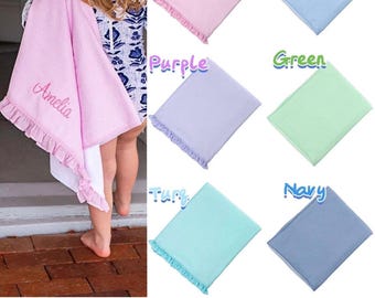 Puede incluir: Toalla de playa rosa con estampado de cuadros vichy seersucker con el nombre "Amelia" bordado. La toalla tiene un borde con volantes. También se muestran otras toallas de colores lisos en azul, morado, verde, turquesa y marino.