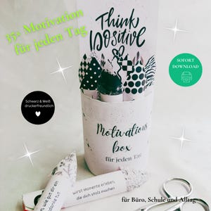 Könnte beinhalten: Eine weiße Motivationsbox mit dem Text "Think Positive" und "Motivation box für jeden Tag". Die Box enthält 35 aufgerollte Notizen mit motivierenden Botschaften. Das Bild enthält auch den Text "35x Motivation für jeden Tag".