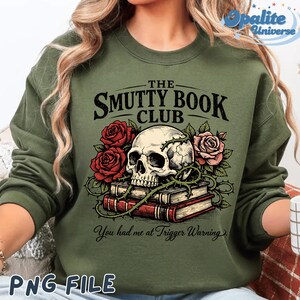 Puede incluir: Sudadera verde oliva con un dise&ntilde;o gr&aacute;fico que presenta una calavera, rosas rojas y rosas, y una pila de libros. El texto dice "THE SMUTTY BOOK CLUB" y "You had me at Trigger Warning."