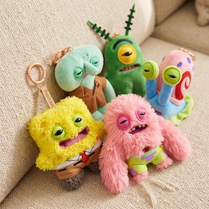 Puede incluir: Colección de peluches estilo Fuggler. Los juguetes incluyen un personaje amarillo con forma de esponja, una criatura rosa y peluda, un extraterrestre verde, un caracol azul y un calamar verde. El juguete amarillo tiene un llavero que dice "Fuggler".
