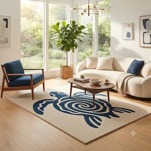 May include: A rectangular area rug featuring a large, stylised dark blue sea turtle graphic with a spiral shell pattern on a cream-coloured background. The rug is positioned in a living room setting with a wooden coffee table, a blue armchair, and a sofa.