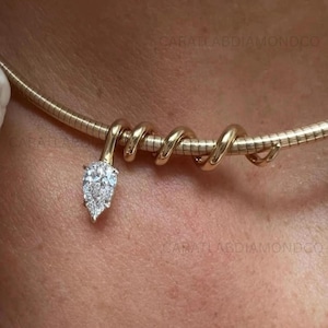 Pode incluir: Um colar de corrente omega de ouro com um design em espiral que envolve a banda, terminando num pendente de diamante em forma de pera. O texto CARATLABDIAMONDCO é visível no fundo. O colar repousa sobre a pele.