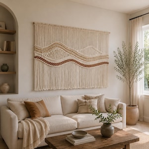 May include: A large rectangular wall hanging made of off-white macrame cord featuring a wave-like pattern with integrated wooden beads and a horizontal band of dark brown woven texture, suspended from a wooden rod against a plain wall.