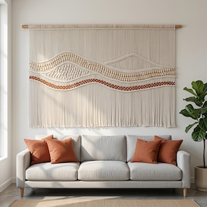 May include: A large macrame wall hanging suspended from a wooden rod, featuring off-white cotton cord, rows of light wooden beads, and a wavy band of terracotta-colored woven fabric, with long fringe extending from the bottom edge.