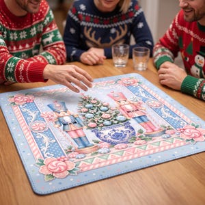May include: A square mat featuring a light blue background with a central illustration of two nutcrackers flanking a decorated Christmas tree in a blue and white patterned pot, surrounded by pink peppermint candies and floral accents.