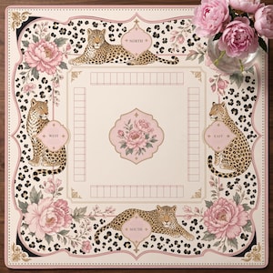 May include: A square board game mat featuring a cream background with a black leopard print border, pink peony floral illustrations, and four leopards positioned at the North, South, East, and West compass points with corresponding text labels.