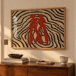 May include: A rectangular framed wall art piece featuring a graphic illustration of two figures in red silhouettes standing against a background of wavy black and beige lines. The figures are wearing hats and one holds a coiled rope in their hand.