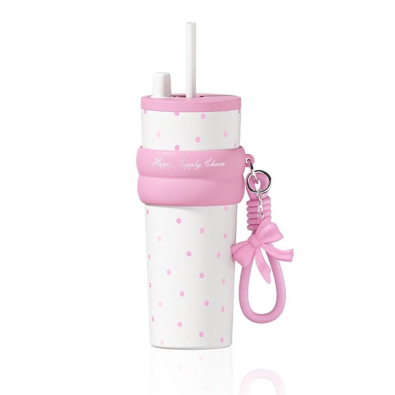 May include: A white tumbler with pink polka dots, a pink lid, and a white straw. A pink silicone band wraps around the center with the text Happy Supply Chain. A pink silicone bow charm hangs from a metal ring attached to the silicone band.