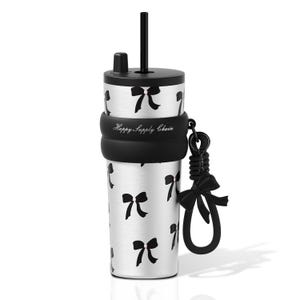May include: A silver stainless steel tumbler featuring a black bow pattern, a black lid with a straw, and a black silicone sleeve printed with the text Happy Supply Chain. A black silicone strap with a decorative bow charm is attached to the side.