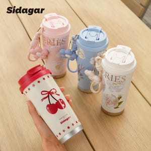 May include: Four insulated travel mugs in pastel colors, each with a flip-top lid and a decorative charm. One mug is held in a hand, featuring a cherry design and the brand name "Sidagar". The other mugs have floral patterns.