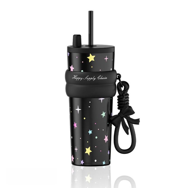 May include: A black tumbler featuring a pattern of colorful pastel stars and dots, a black lid with a straw, and a black silicone sleeve printed with the text Happy Supply Chain. A black cord with a decorative bow is attached to the side of the sleeve.
