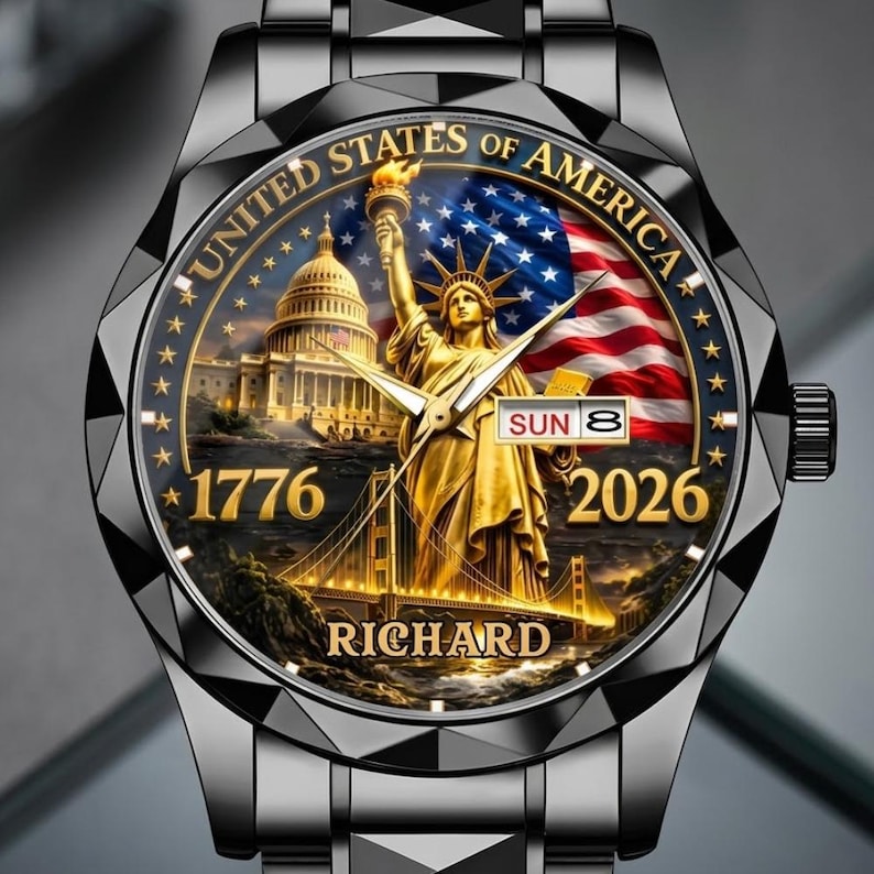 May include: A black wristwatch with a detailed face featuring the Statue of Liberty, the U.S. Capitol, and the American flag. The watch face includes the text "UNITED STATES OF AMERICA", "1776", "2026", and "RICHARD". The watch has a black metal strap.
