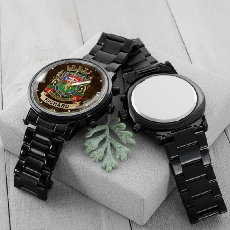 May include: Two black watches with matching bands. One watch face displays a crest with the name "RICHARD" on a banner. The other watch face is plain white. The watches are on a light gray surface.